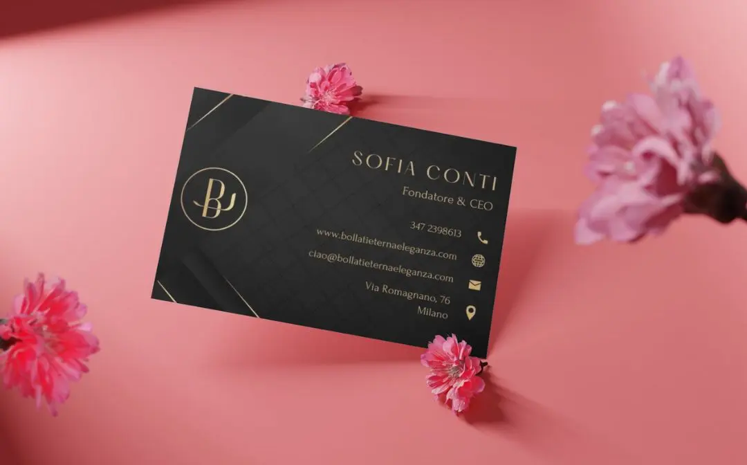 Un biglietto da visita nero con testo dorato e contiene le informazioni di contatto, posizionato su uno sfondo rosa con fiori rosa