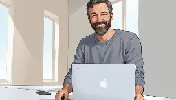 Un hombre caucásico de mediana edad con barba y cabello rizados, vestido con un suéter gris, sentado en un escritorio y usando una computadora portátil